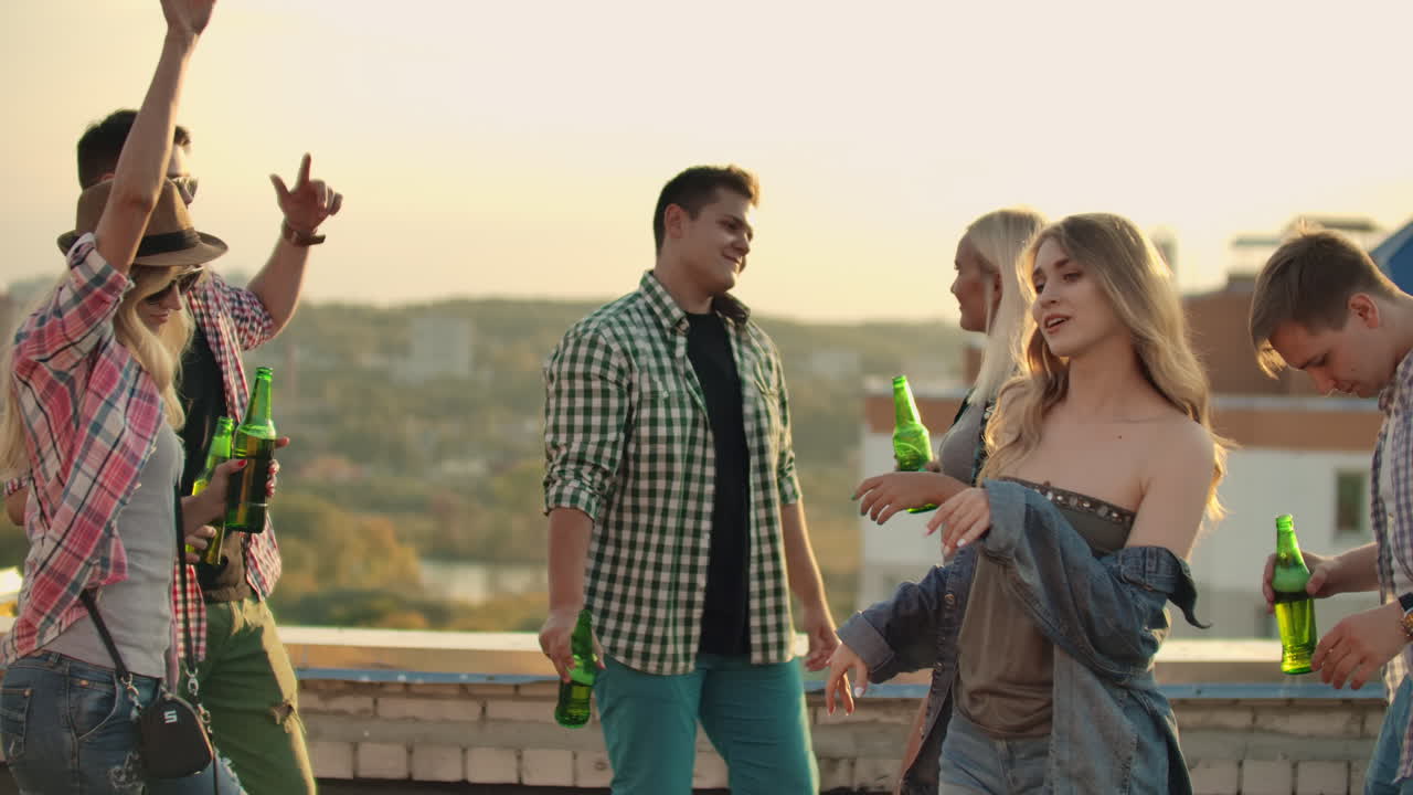 A company of six young people threw a party on the roof. This is dancing fun and communication between friends with beer in plaid shirts and shorts in the summer.