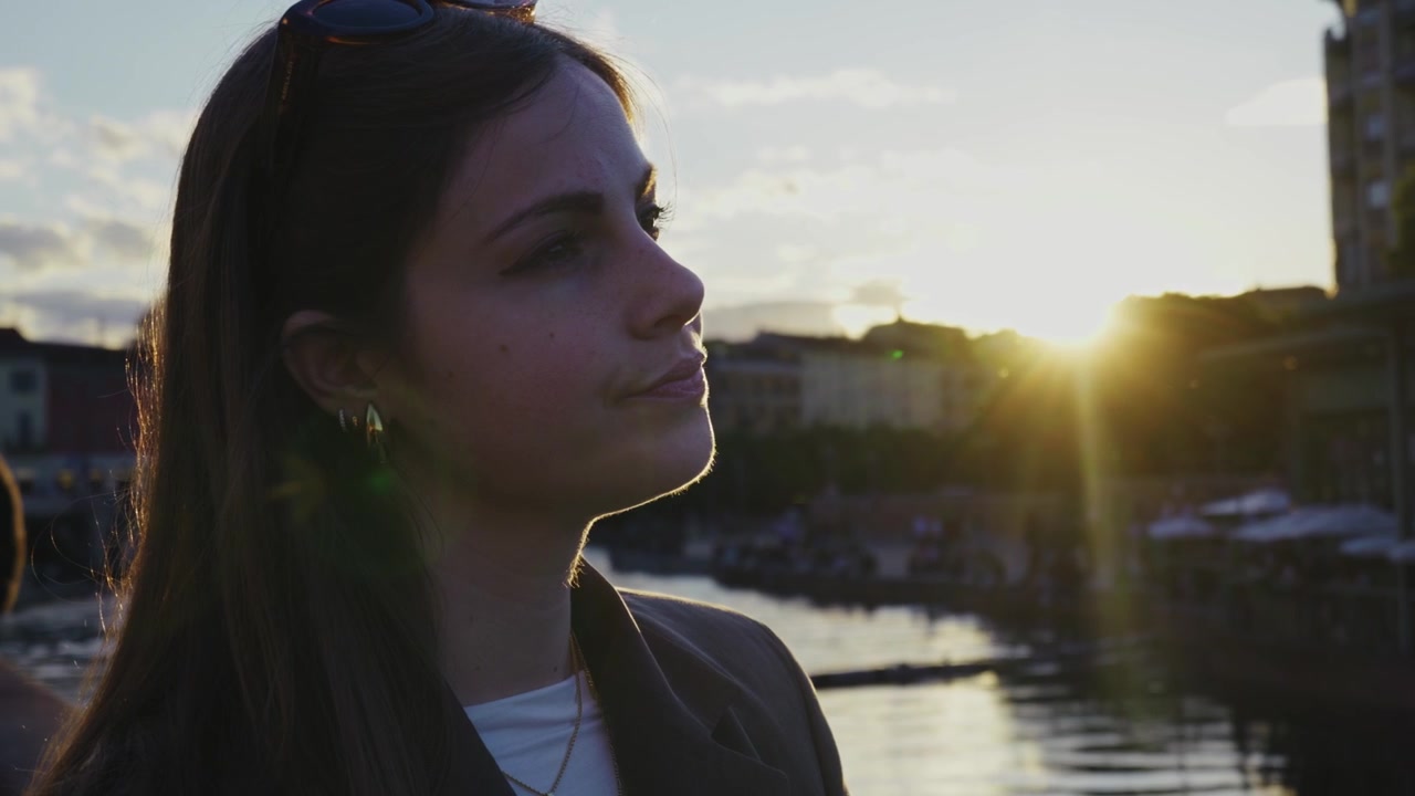 Retrato de uma jovem mulher desfrutando da luz do pôr do sol perto da orla em Milão, criando uma atmosfera de estilo de vida urbano cinematográfica e acolhedora.