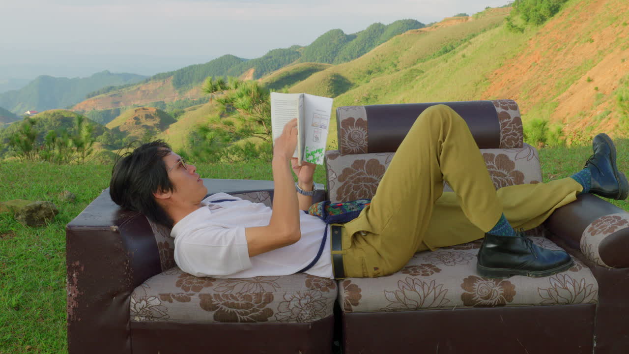 young student reading a book while laid on outdoor sofa couch in nature