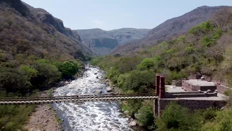 drone aéreo volando sobre un puente colgante a lo largo de un río en el parque nacional barranca de huentitan en méxico