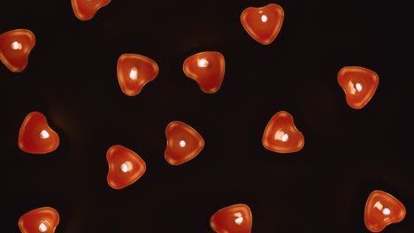 overhead shot of romantic lit heart shaped red candles revolving on black background