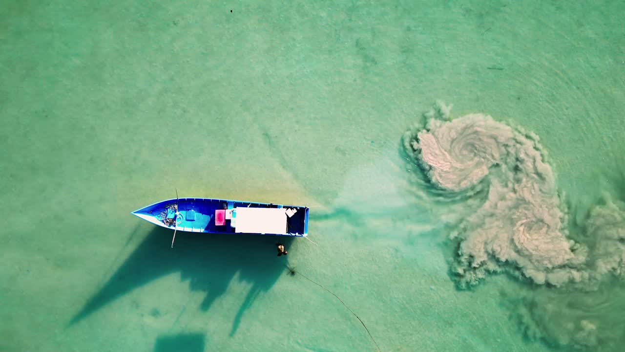 바가에 어져 있는 파란색 물 위에 떠다니는 배의 공중 사진 - 바가의 모래 물에서 배가 오염시키면서 해안선 근처에 어진 잔해가 있습니다.