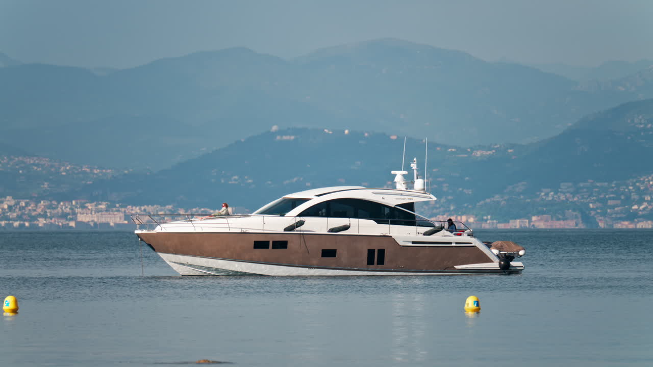 Antibes, France - May 6, 2025: People on a boat docked on the sea with the city and mountains on the background in daylight