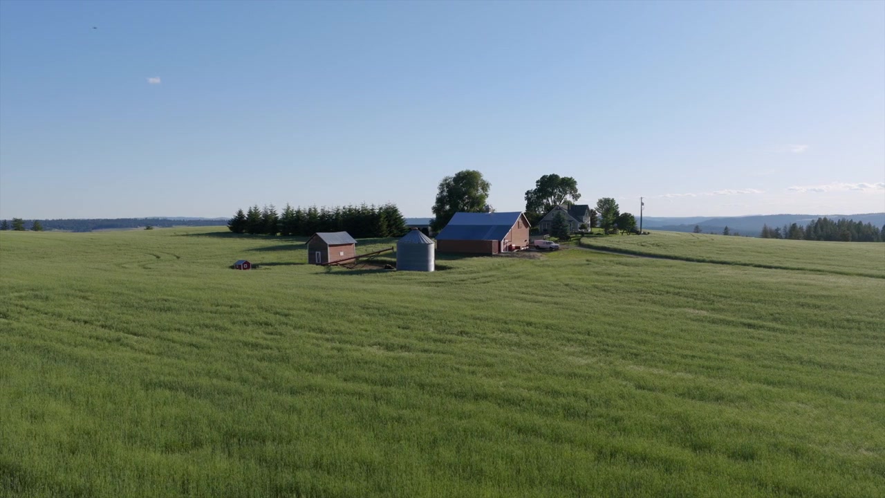 Nærbillede fra luften af en landejendom nær Spokane, WA, med lader, en kornsilo og omkringliggende grønne afgrødemarker