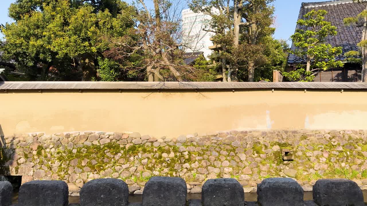 明るい日差しの下、歴史的な土壁と石の基礎をゆっくりとしたパンショットで捉えています。