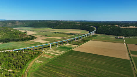 aerial view of a long bridge spanning a green valley with fields and forests