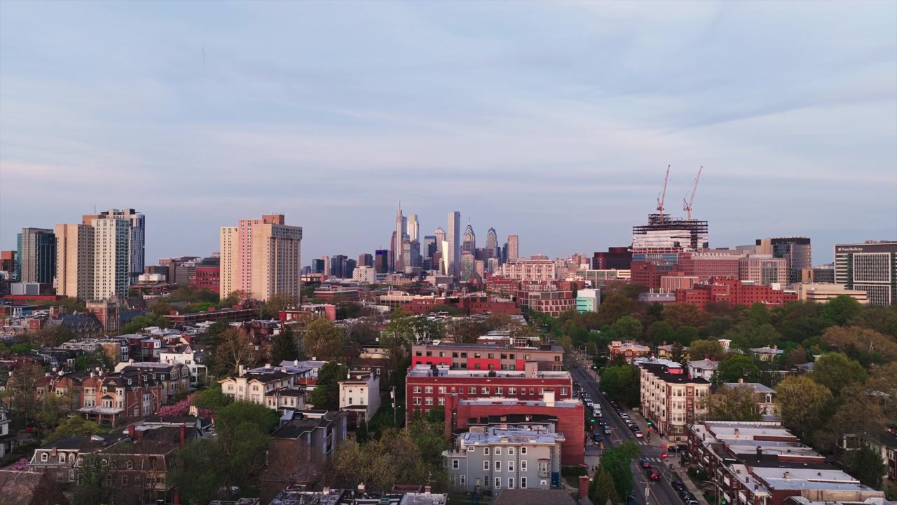 Vista aerea con drone delle case a schiera di West Philadelphia e della chioma degli alberi che si estende verso lo skyline del centro di Philadelphia al tramonto con gru edili attive