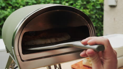 close-up launching a freshly homemade margarita pizza into a small pizza oven