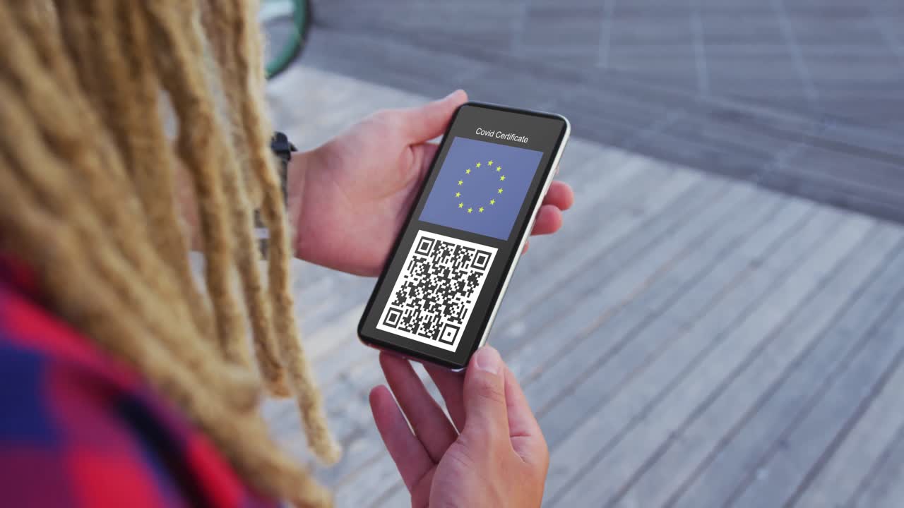 Man with dreadlocks holding smartphone, covid vaccination certificate, eu flag and qr code on screen