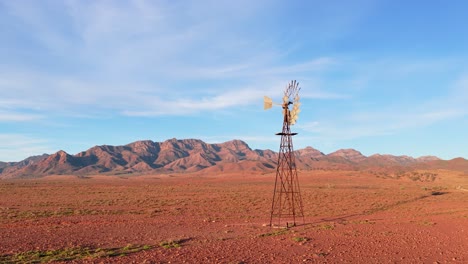 Drone orbit around windmill against rugged Flinders Ranges mountains in red outback, South Australia
