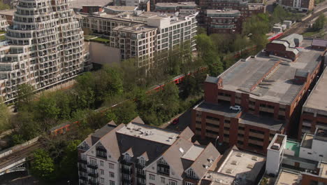 Red-passenger-train-flying-through-cityscape-landscape,-aerial-follow-view