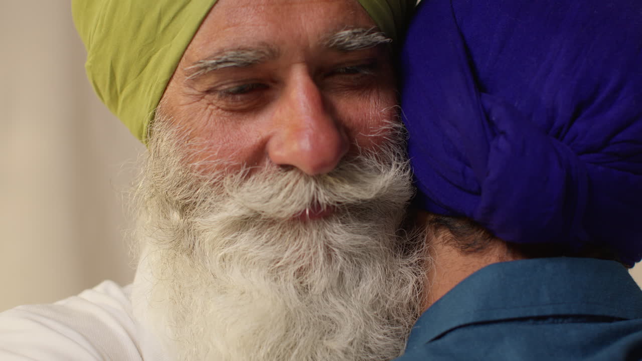 dos hombres sikhs se abrazan afectuosamente, el hombre mayor sonriendo cálidamente y el joven mirando hacia abajo.
