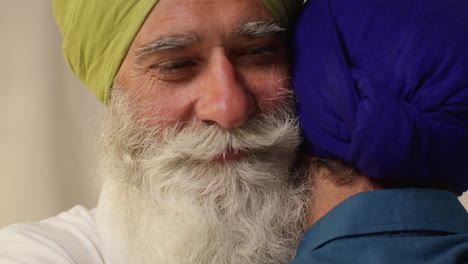 dos hombres sikhs se abrazan afectuosamente, el hombre mayor sonriendo cálidamente y el joven mirando hacia abajo.