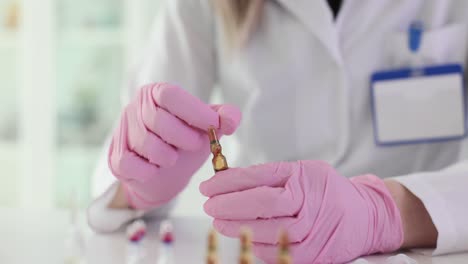 scientist in pink gloves holding an ampoule in a lab