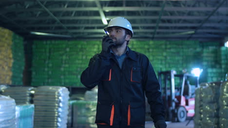 male warehouse worker using walkie-talkie and inspecting blueprints