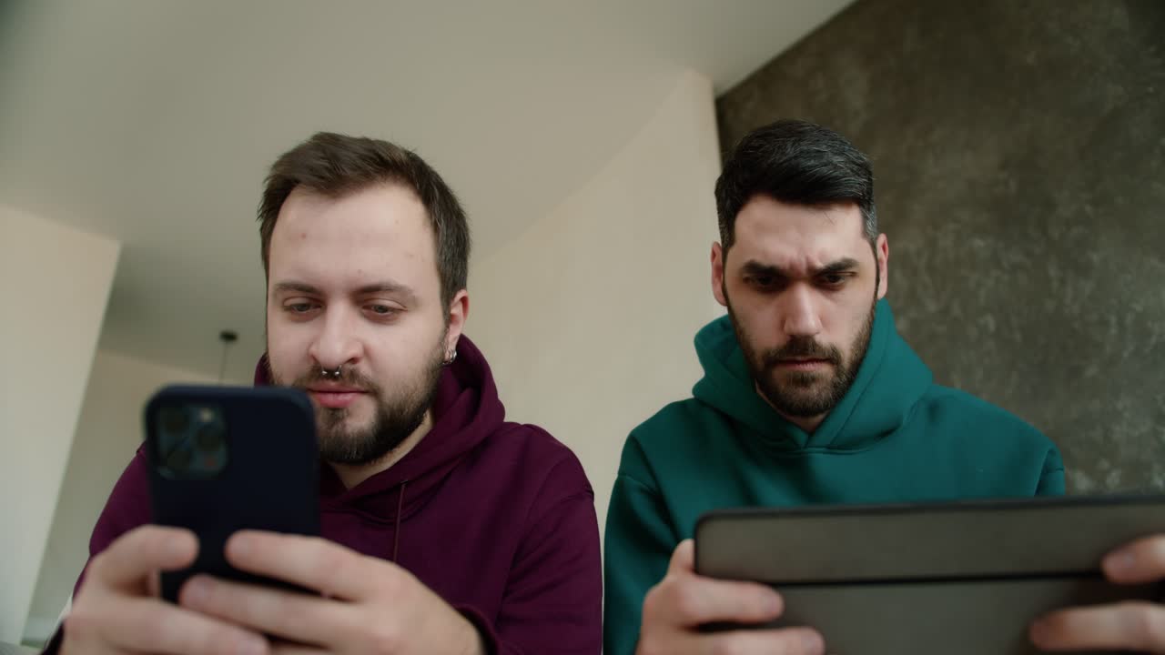 joven pareja gay lgbtq usando teléfono móvil y tableta jugando juegos en internet juntos