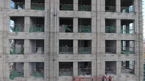 Workers-on-a-building-on-construction-aerial-drone-shot-going-up-and-discovering