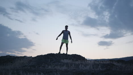 Athletic-man-silhouetted-against-evening-sky-walking-on-hill-or-mountain-top