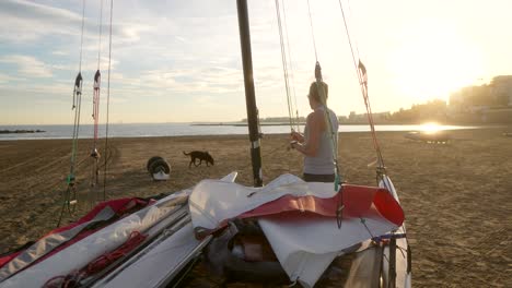 Hombre-Preparando-Catamarán-En-La-Playa-Por-La-Mañana-Con-El-Sol-Saliendo