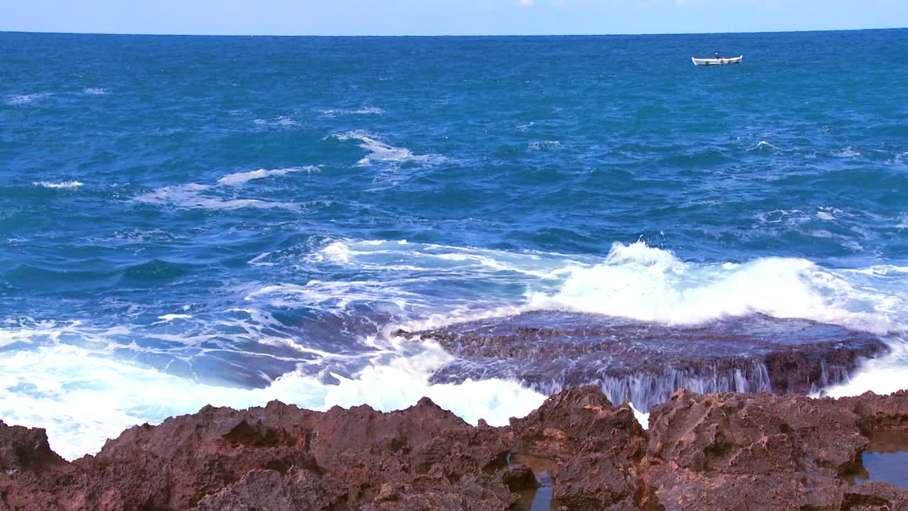 멀리 떨어진 작은 어선과 함께 해안선에 부서지는 파도의 넓은 샷