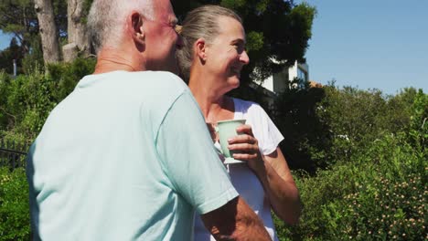 Caucasian-senior-couple-holding-coffee-cup-talking-to-each-other-in-the-balcony-at-home