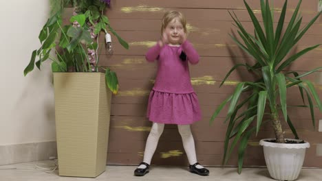 little child dance near flowerpots and wooden fence. feel happy, smiling