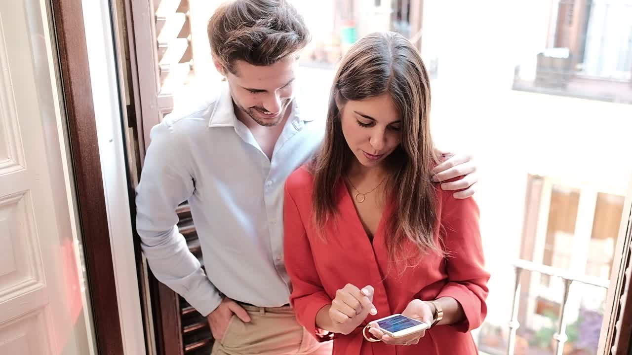 Pareja joven sonriente usando un smartphone en casa