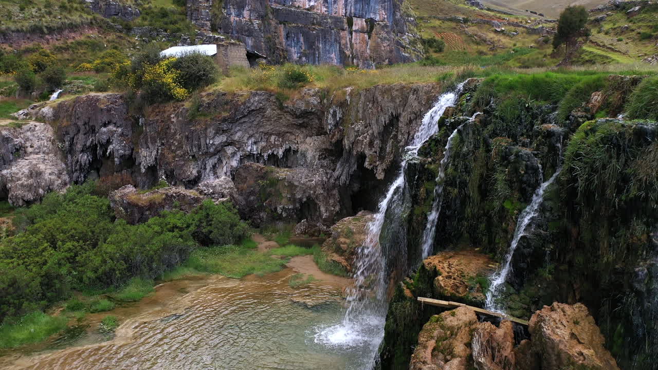 hermosa toma de un dron de una cascada natural al lado del lago millpu de aguas turquesas con mucha vegetación y montañas alrededor en un día nublado