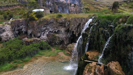 hermosa toma de un dron de una cascada natural al lado del lago millpu de aguas turquesas con mucha vegetación y montañas alrededor en un día nublado