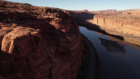 aerial view of golden hour sunlight above red sandstone cliffs and colorado river, moab utah usa