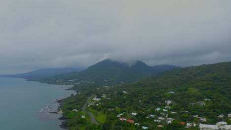 Aerial-footage-traveling-to-the-left-above-a-tropical-cityscape-with-lush-forested-hills-and-a-coastal-beachfront-on-a-rainy-day