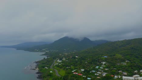 imágenes aéreas que viajan hacia la izquierda sobre un paisaje urbano tropical con exuberantes colinas boscosas y una playa costera en un día lluvioso