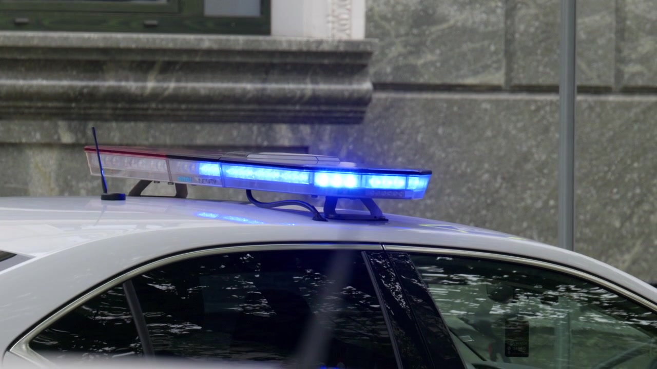 Nahaufnahme von blinkenden roten und blauen Einsatzlichtern auf einem Polizeiauto in einer städtischen Straßenumgebung.