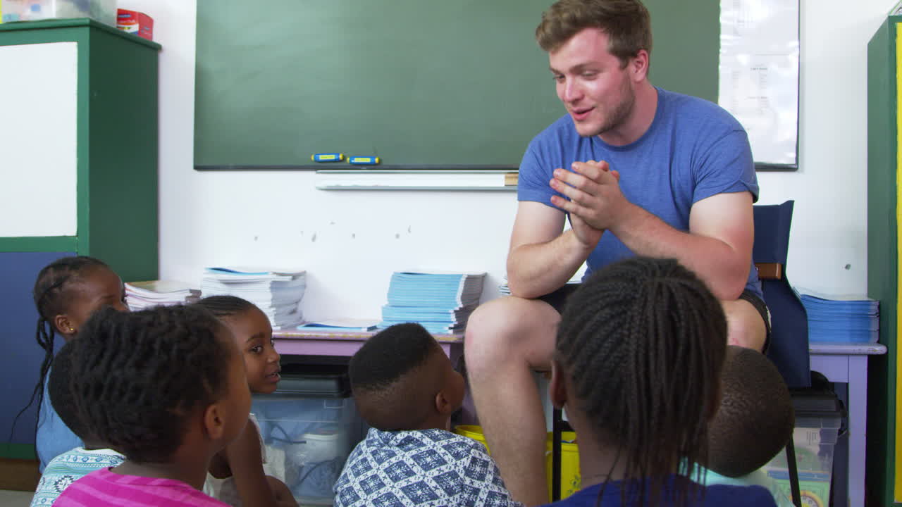 School kids sitting on floor clapping hands with teacher