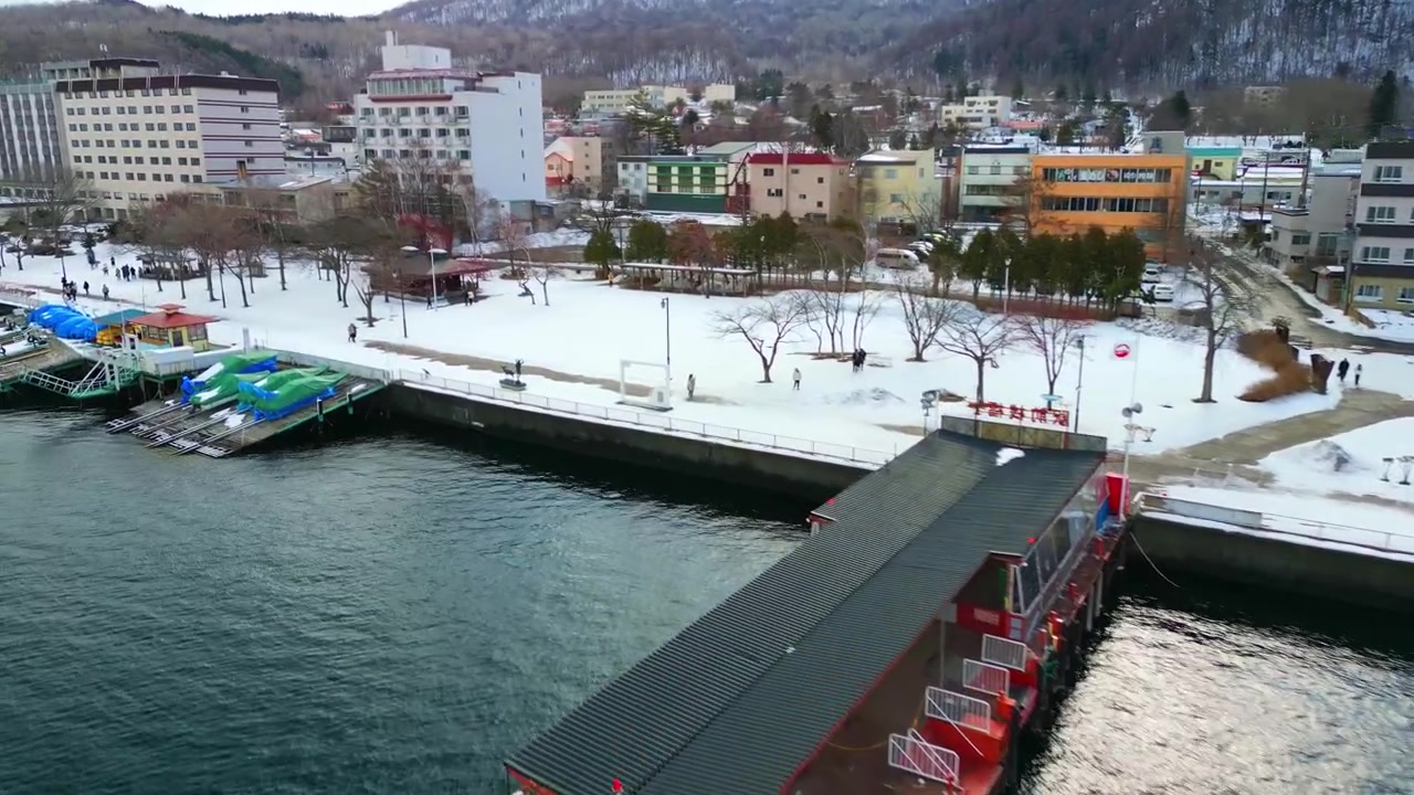 Hokkaido'da kış mevsiminde Toya Gölü'nün karlı gezinti yolunda yürüyen yayalar ve üstü kapalı bir iskelenin tepeden hava görünümü