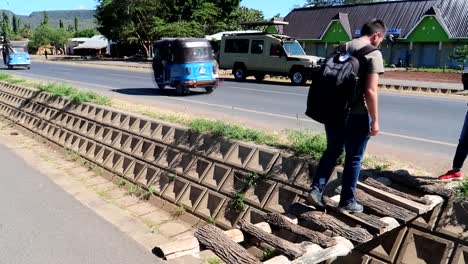 Plano-Completo-Del-Hombre-Cruzando-Un-Puente-De-Madera-Hecho-A-Mano-En-Arusha-Tanzania,-Calle-Transitada