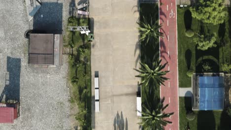 Top-down-view-of-people-walking-on-beach-boulevard,-casting-long-shadows-on-ground,-Aerial