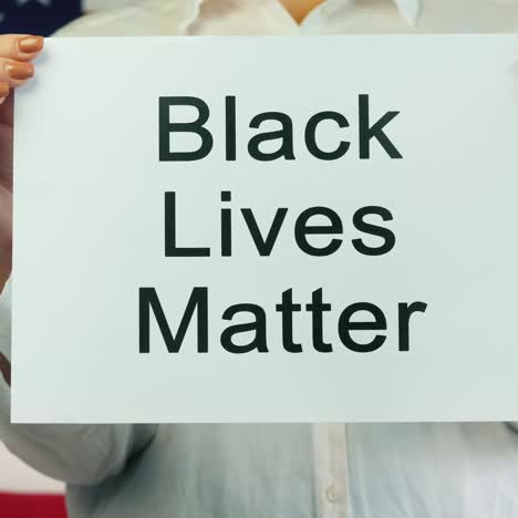 woman holds poster stating black lives matter with an american flag background