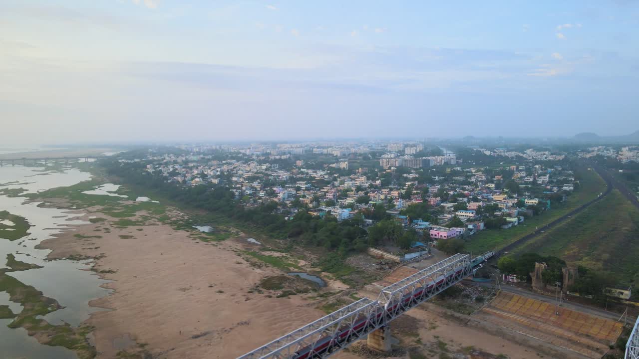 Aerial drone shot capturing an Indian train as it moves swiftly through the heart of the city, showcasing the urban rhythm.
