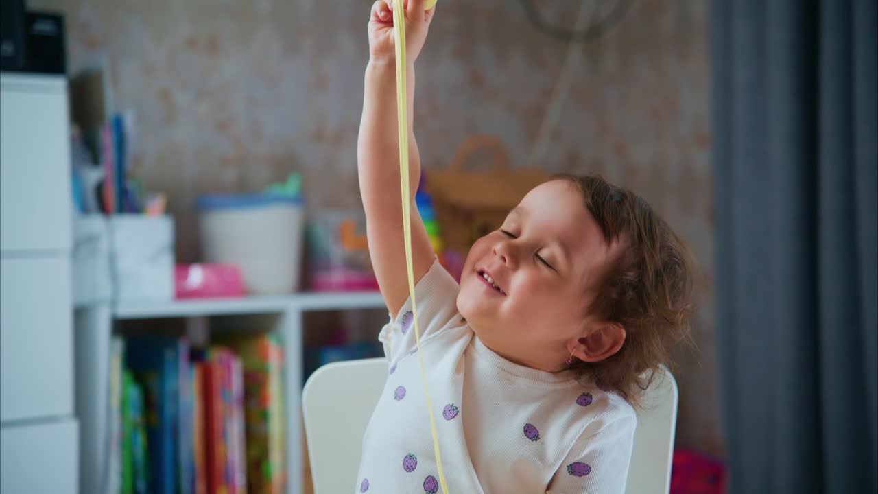 A Curious Child's Joyful Exploration of Stretchy Slimy Substance: A Playful Encounter with Gooey Fun in a Colorful Indoor Setting