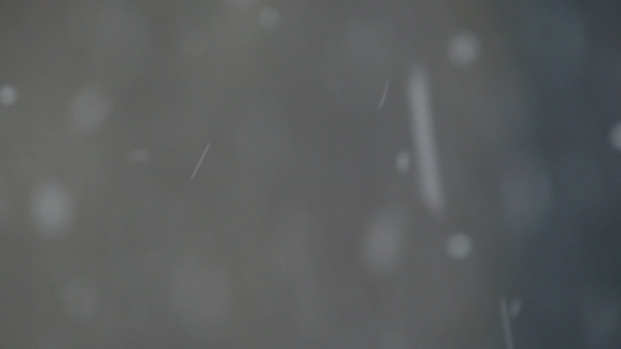 Primo piano estremo di fiocchi di neve in una giornata nevosa su uno sfondo scuro e sfocato.