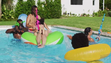 Diverse-group-of-friends-having-fun-playing-with-water-guns-on-inflatables-in-swimming-pool