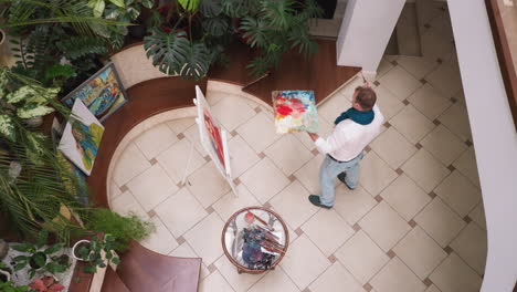 man swirls around canvas with portrait in studio hall. happy artist executes strokes with paint brush while dancing in art studio. infusing life in masterpiece