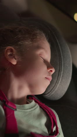 una vista de cerca de un niño durmiendo pacíficamente en un asiento de coche por la noche, el niño está usando un mono rosa y una camisa verde claro, descansando cómodamente contra el asiento del coche