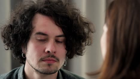 Over-his-shoulder-a-sad-brunette-guy-with-curly-hair-and-a-mustache-listens-to-a-brunette-girl-dissatisfaction-with-him-at-home