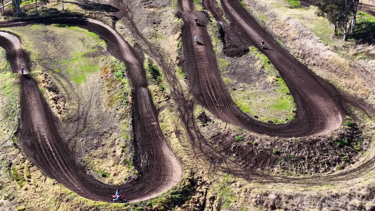 Multiple dirt bikes speed along winding motocross track, aerial view, bright daylight, dynamic movement