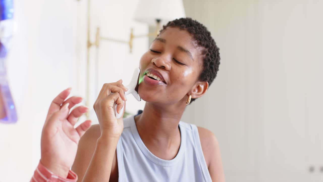 Woman receiving treatment at home vanity, holding device while tech guiding as green LED lighting