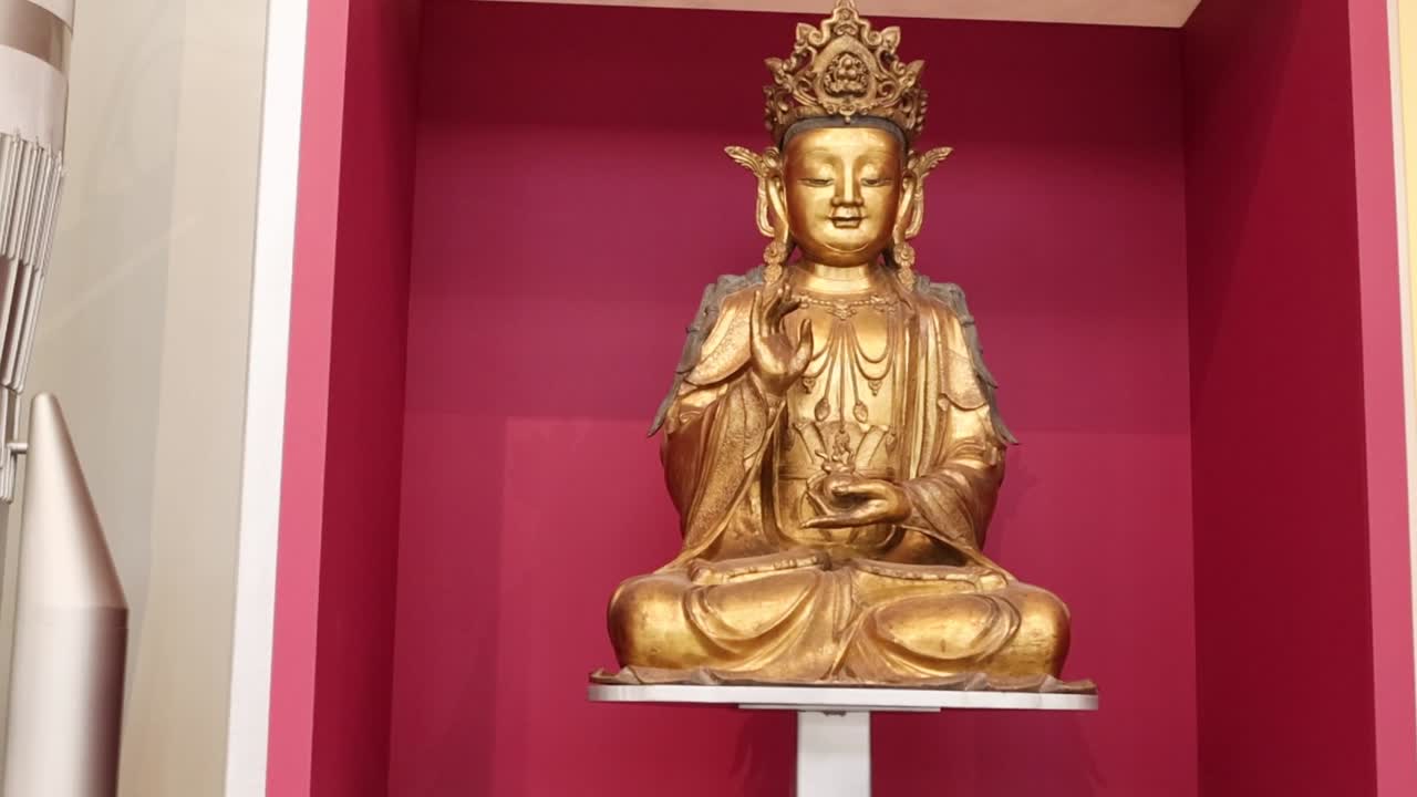 A detailed view of a golden Buddha statue seated against a vibrant red backdrop.