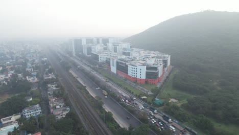 Aerial-Drone-Shot-Of-Misty-View-Of-Corporate-Buildings-Near-A-Highway-With-Cars-Passing-By