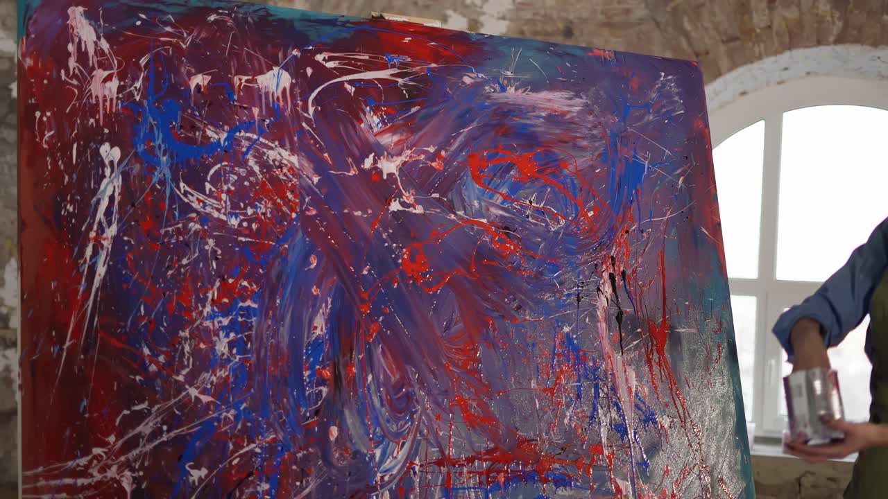 mujer pinta en lienzo sumergiendo las manos en frasco de pinturas